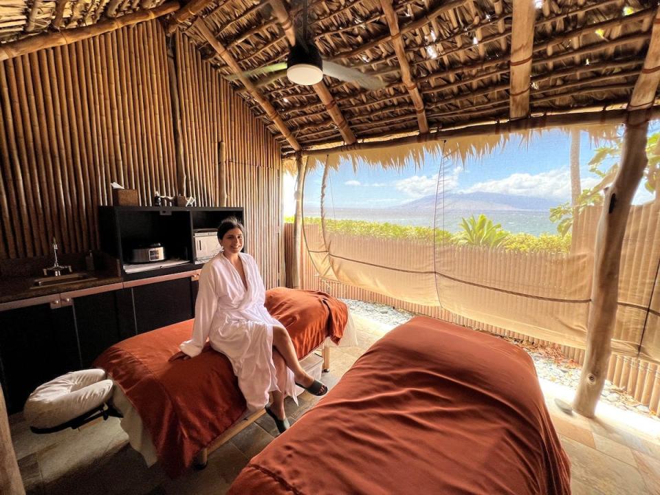 A woman sits on a massage bed in a massage hale (a hut) by the beach at the Four Seasons Maui at Wailea.