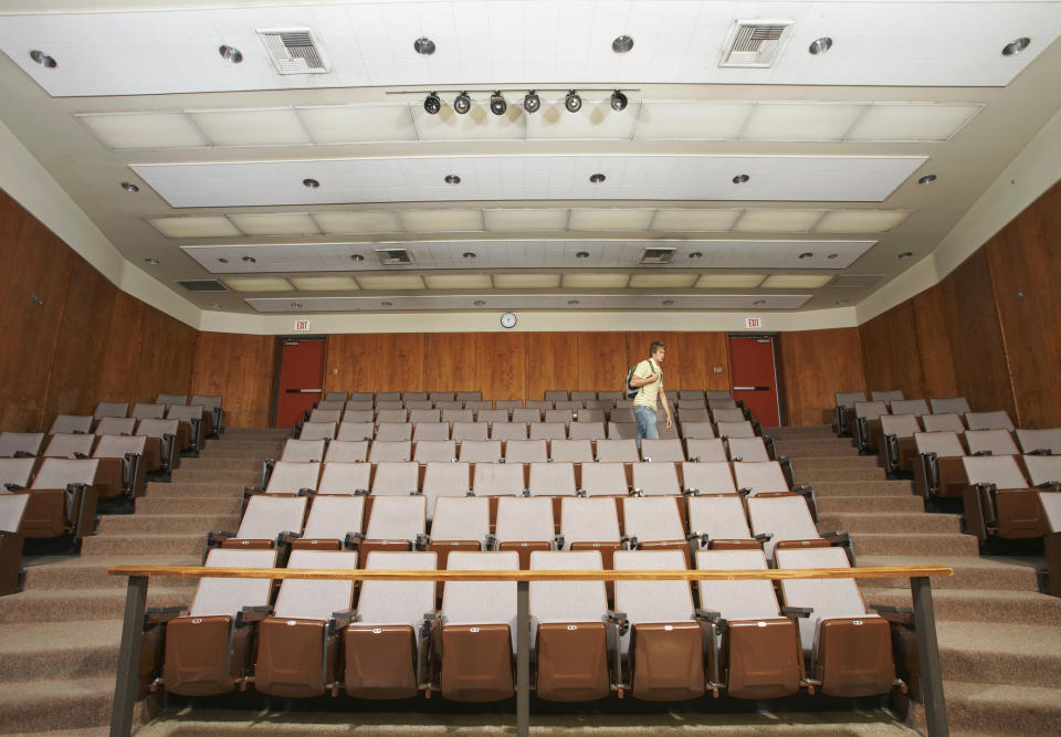 Person standing in the aisle of an empty lecture hall looking at their phone