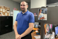 988 Call Center Director Jamieson Brill poses for a photo in front of a desk where work workers take calls around the clock at a facility in Hyattsville, Md., Oct. 7, 2022. Brill works in one of more than 200 call centers fanned out around the country tasked with answering an uptick in calls around the clock from people considering suicide or experiencing a mental health emergency. (AP Photo/Amanda Seitz)