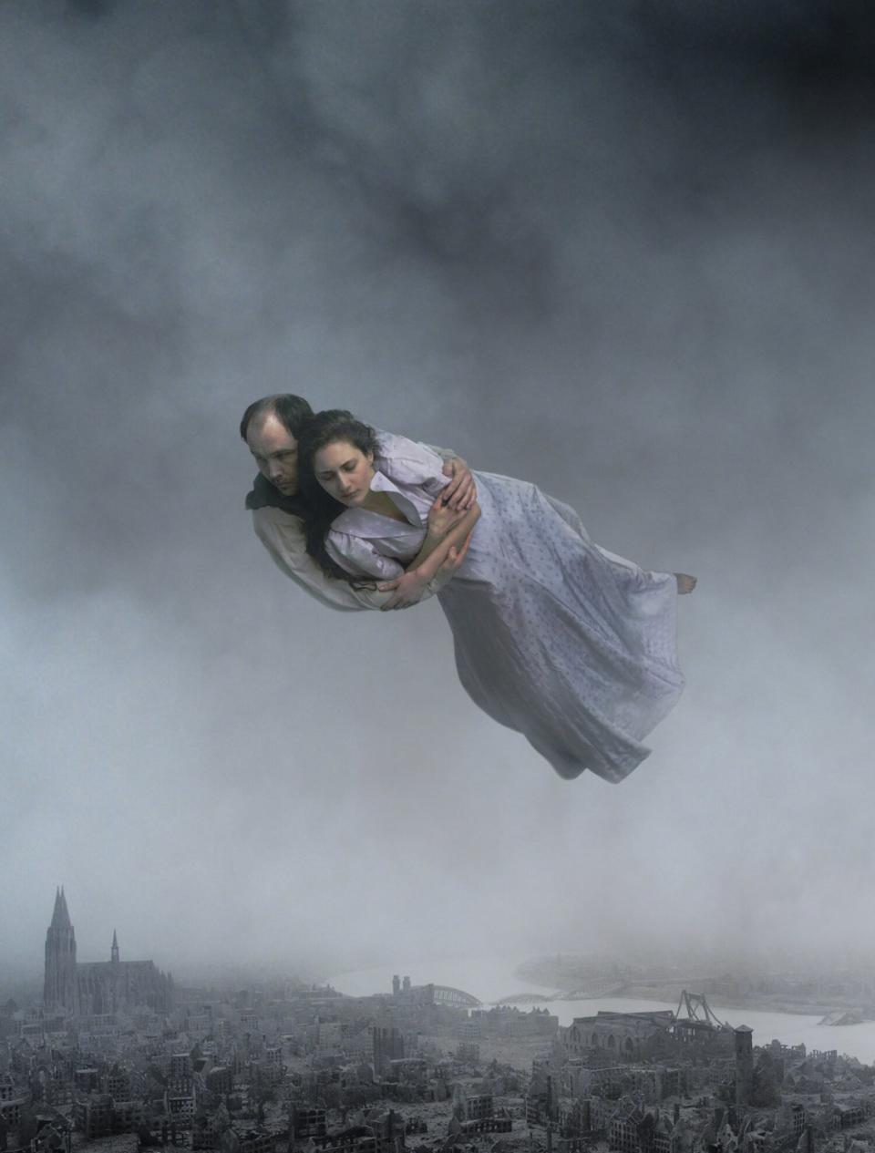 A scene of a man holding a woman while flying above a city from the movie "About Endlessness."