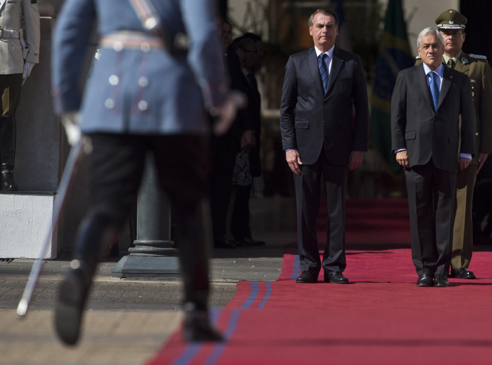 Brazil's President Jair Bolsonaro, left, and Chilean President Sebastian Pinera, receive military honors in front of the presidential palace La Moneda,in Santiago, Chile, Saturday, March 23, 2019. Bolsonaro is on the second day of his two-day visit. (AP Photo/Esteban Felix)