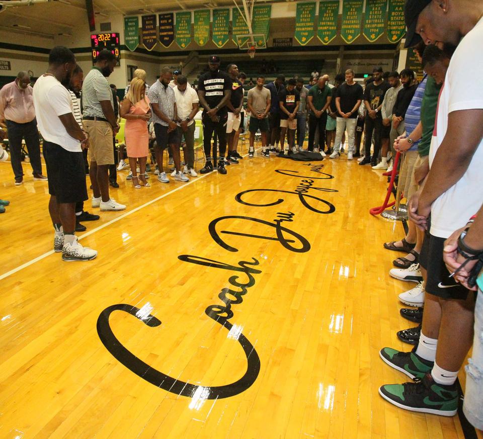 Former St. Vincent-St. Mary High School basketball players who played for coach Dru Joyce II bow their heads in prayer around Joyce's name on the court during the benediction of the court's dedication ceremony Sunday at The LeBron James Arena.