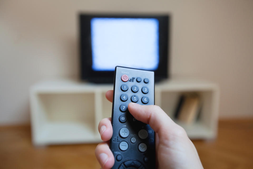 A hand holding a television remote and a TV showing static