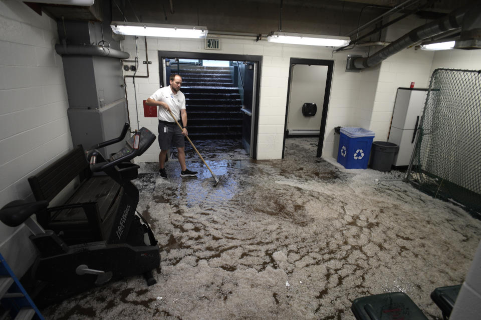 Water and hail flood the entrance to the visitor's dougout as a cloubhouse attendant tries to clean up the mess left after a summer storm packing heavy rain, high winds and large hail swept over Coors Field, Thursday, June 29, 2023, in Denver. The Colorado Rockies were set to host the Los Angeles Dodgers, Thursday. (AP Photo/David Zalubowski)
