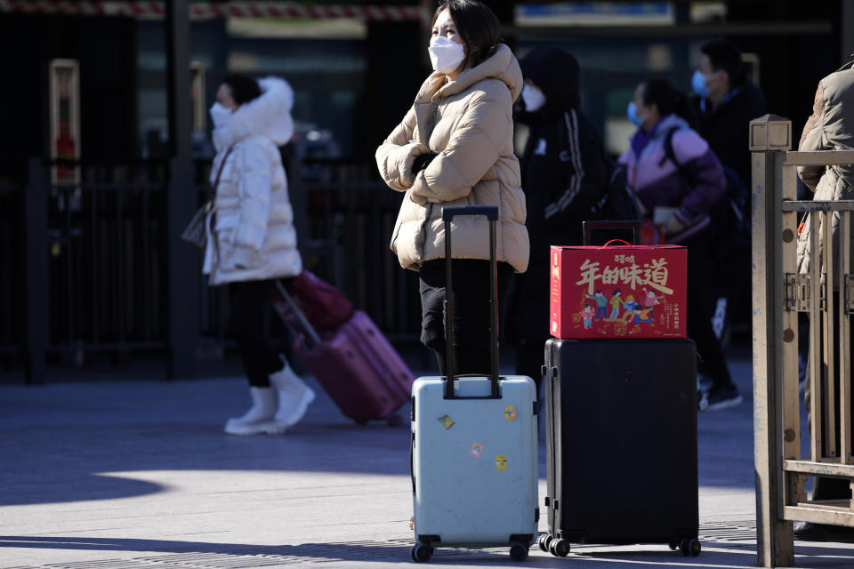 A traveler waits outside the Beijing railway station with her trolley bags and a gift box with the words "The taste of New Year" in Beijing, China, Friday, Jan. 28, 2022. The Beijing Winter Olympics is coinciding with the Chinese Lunar New Year and renewed Covid outbreaks prompting the Chinese authorities to call on the public to stay where they are instead of traveling to their hometowns for the year's most important family holiday. (AP Photo/Ng Han Guan)
