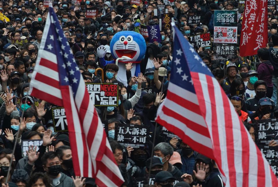 Hong Kong people wave the U.S flags and display a model of Doraemon during their annual pro-democracy march on New Year's Day to insist their five demands be matched by the government in Hong Kong, Wednesday, Jan. 1, 2020. The five demands include democratic elections for Hong Kong's leader and legislature and a demand for a probe of police behavior during the six months of continuous protests. (AP Photo/Vincent Yu)