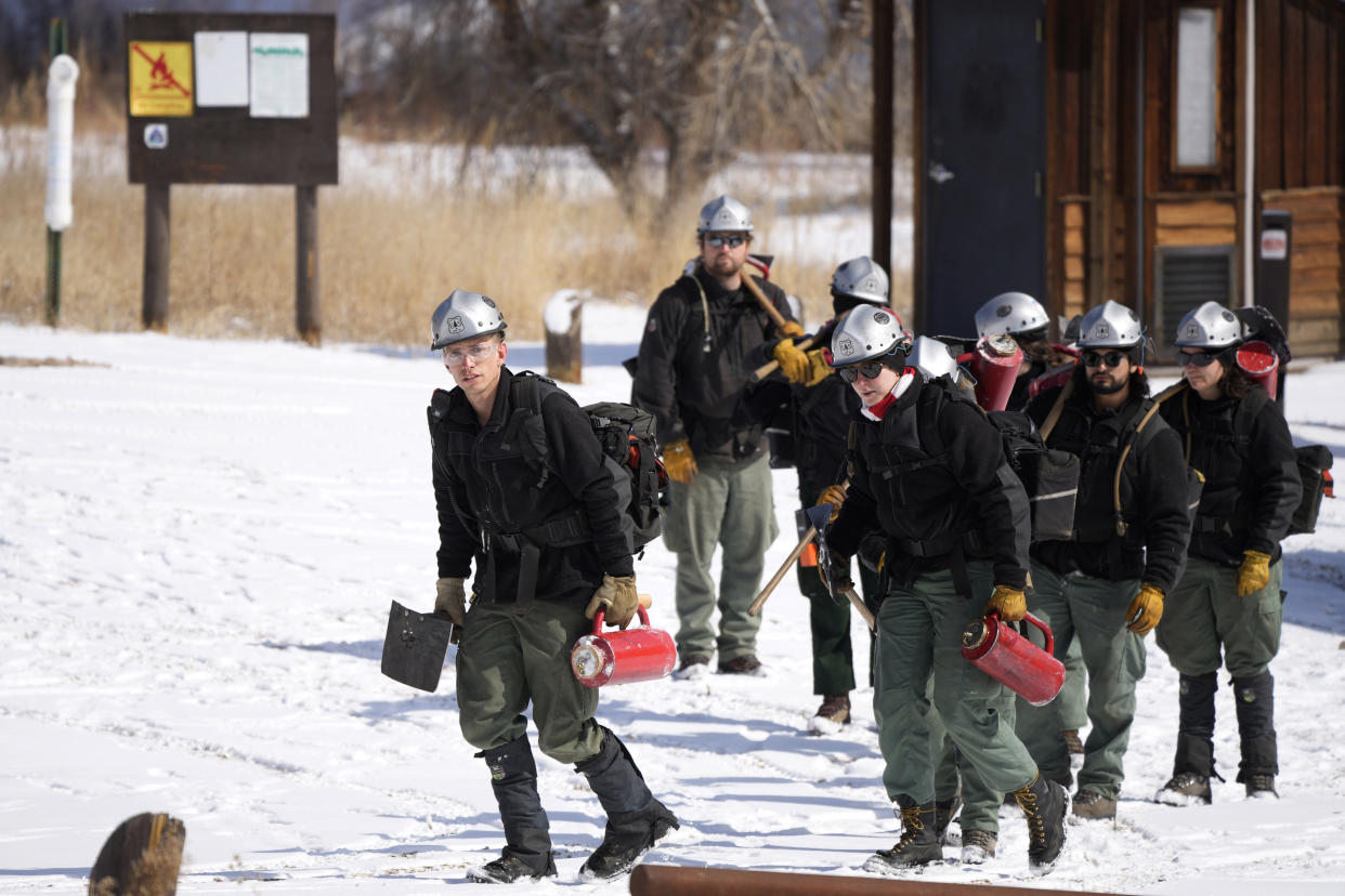 Mile High Youth Corps member John Knudsen leads a group of firefighters to set fire to piles of tree debris alongside U.S. Forest Service firefighters near the Bridge Crossing picnic grounds in Hatch Gulch Wednesday, Feb. 23, 2022, near Deckers, Colo. In Colorado, climate change means snow is not always on the ground when needed so that crews can safely burn off debris piles and vegetation to help keep future wildfires from becoming catastrophic. (AP Photo/David Zalubowski)