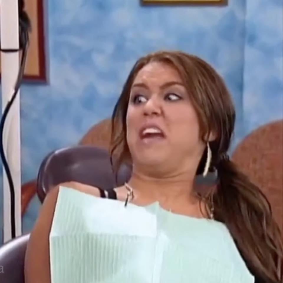 Miley Cyrus sits in a dental chair, looking horrified with a giant syringe held up by a dentist