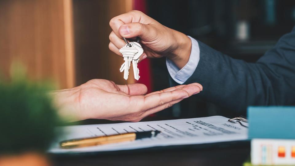 estate agent giving house keys to woman and sign agreement in office.