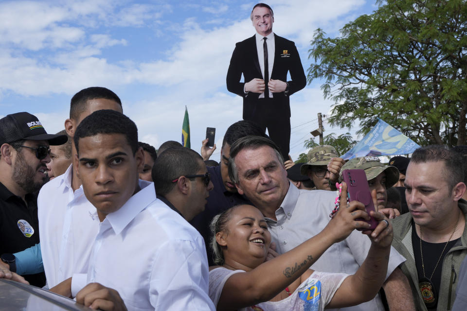 Brazil's President Jair Bolsonaro, center, poses for a selfie with a supporter as he campaigns for reelection at the rural workers' settlement New Jerusalem, in Brasilia, Brazil, on Oct. 24, 2022. (AP Photo/Eraldo Peres)