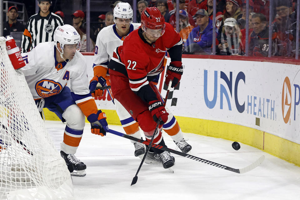 Carolina Hurricanes' Brett Pesce (22) tries to clear the puck with New York Islanders' Cal Clutterbuck (15) and Hudson Fasching (20) nearby during the first period of an NHL hockey game in Raleigh, N.C., Saturday, Dec. 23, 2023. (AP Photo/Karl B DeBlaker)