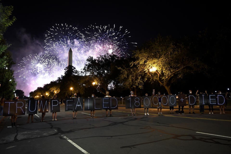 Manifestantes en Washington DC portan una leyenda crítica contra el presidente Donald Trump, que señala la tragedia que ha provocado el covid-19, mientras fuegos artificiales celebran la nominación de Trump al final de la Convención Republicana.(Caroline Brehman/CQ-Roll Call, Inc via Getty Images)