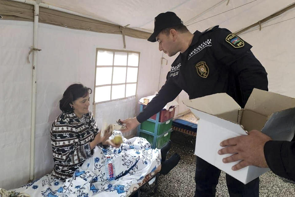 In this photo released by the Azerbaijani Interior Ministry press service on Friday, Sept. 22, 2023, an Azerbaijani police officer gives food to an ethnic Armenian woman in a camp in Khojaly, settlement in Nagorno-Karabakh, Azerbaijan. (Azerbaijani Interior Ministry press service via AP)