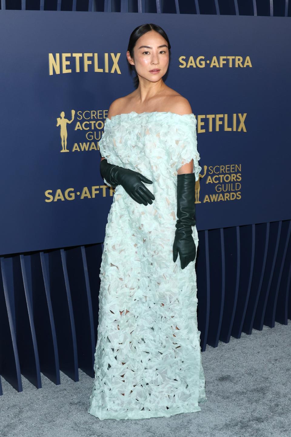 Greta Lee in a mint green lace dress with dark green gloves