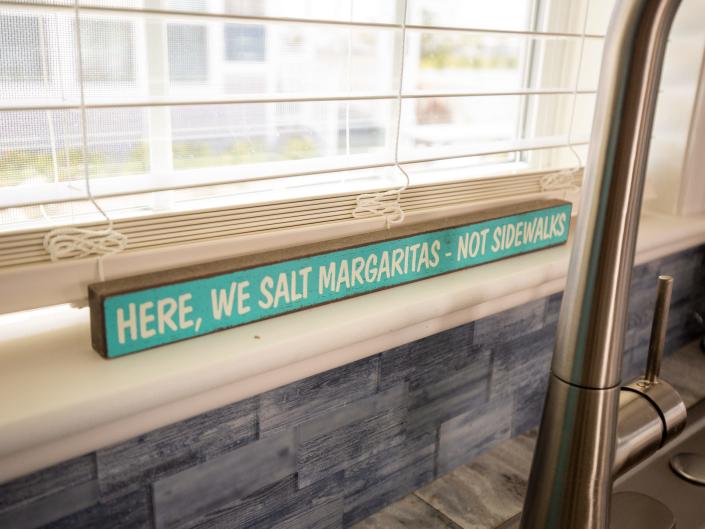 A sign that says &quot;Here, we salt margaritas not sidewalks&quot; under a window.