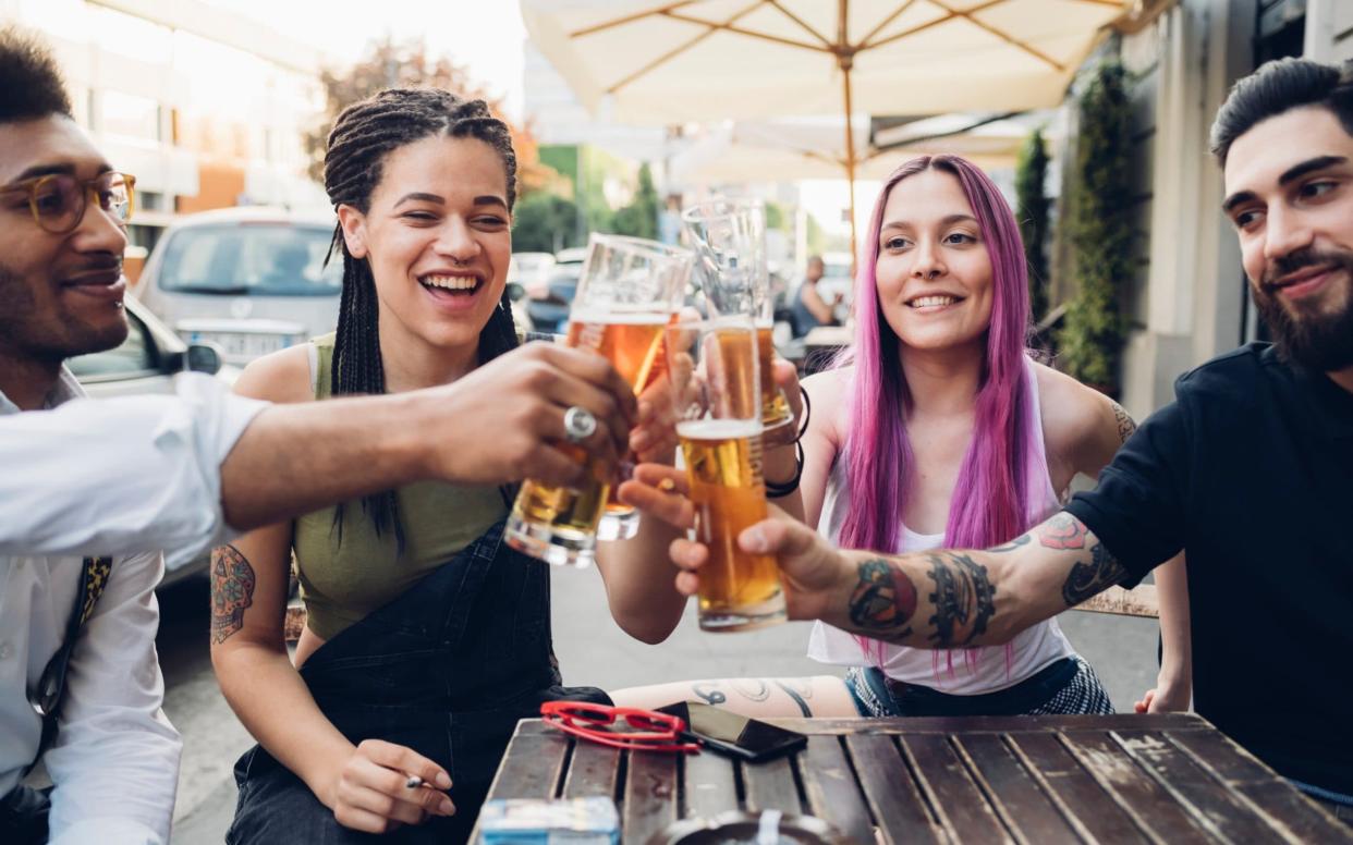 Happy friends clinking beer glasses outdoors at a bar  - Westend61