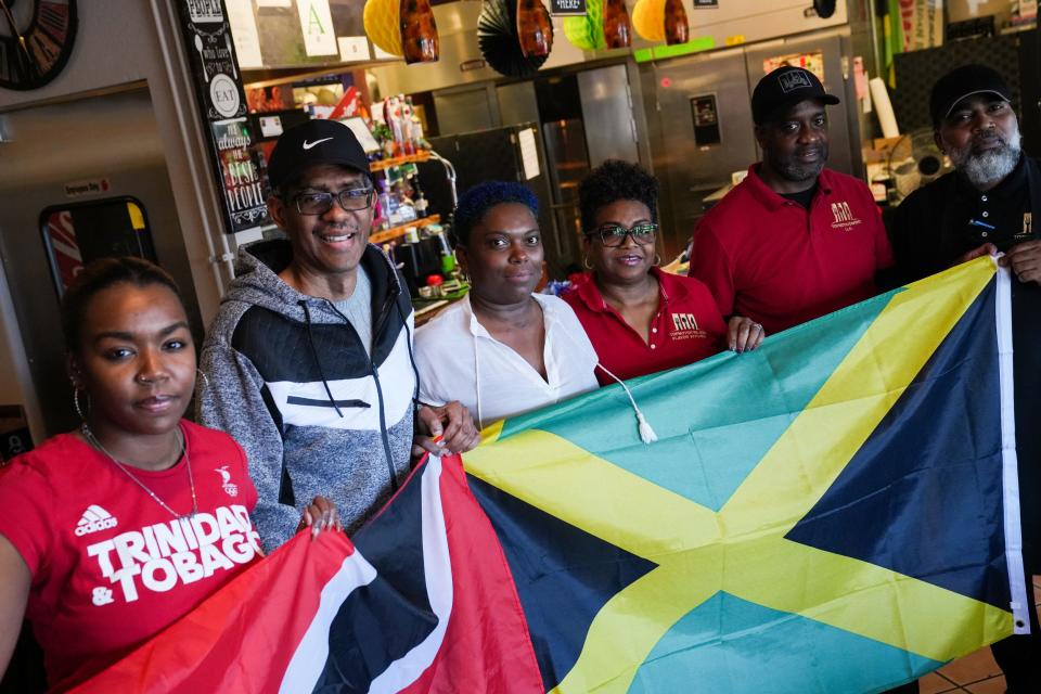 From left; Irma Banzi, Robert Cumberbatch, Margo Laing Wint, Gayle Reid, Curtis Reid and Shernie Gayle pose in front of the flags of Trinidad and Tobago and Jamaica after talking about their experiences as Afro Caribbeans in Arizona at Topnotch Island Flavor Kitchen on Feb. 4, 2023, in Phoenix.