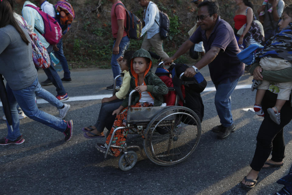 Un migrante, parte de una caravana que se dirige a la frontera entre México y Estados Unidos, empuja la silla de ruedas de un menor por la carretera en Escuintla, Chiapas, México, el sábado 20 de abril de 2019. (AP Foto/Moisés Castillo)