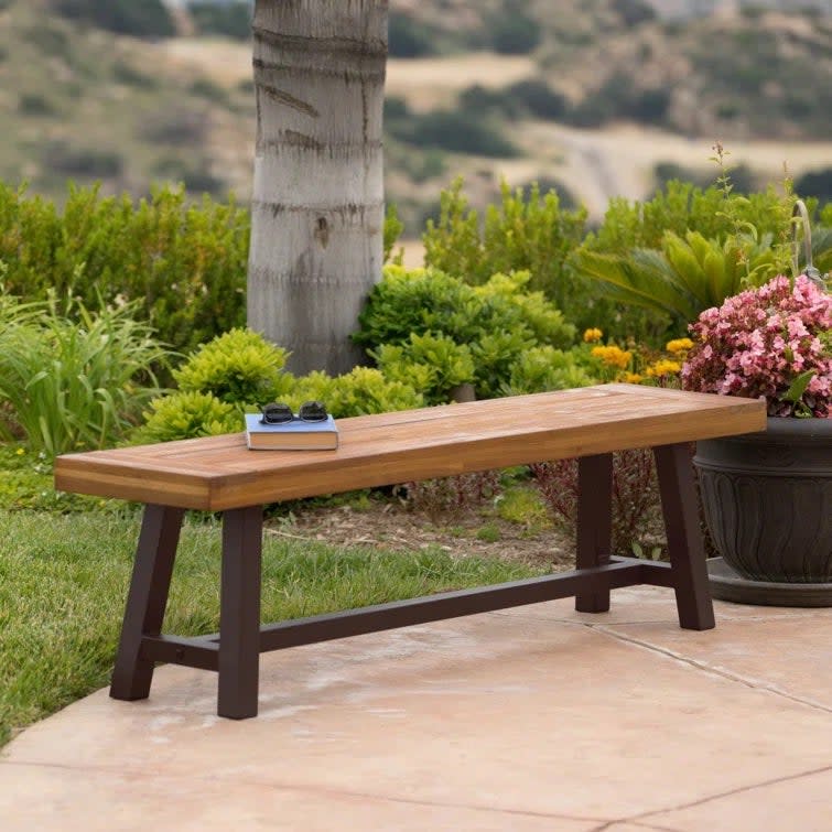 Basic wooden garden bench holding a book and sunglasses on a patio.