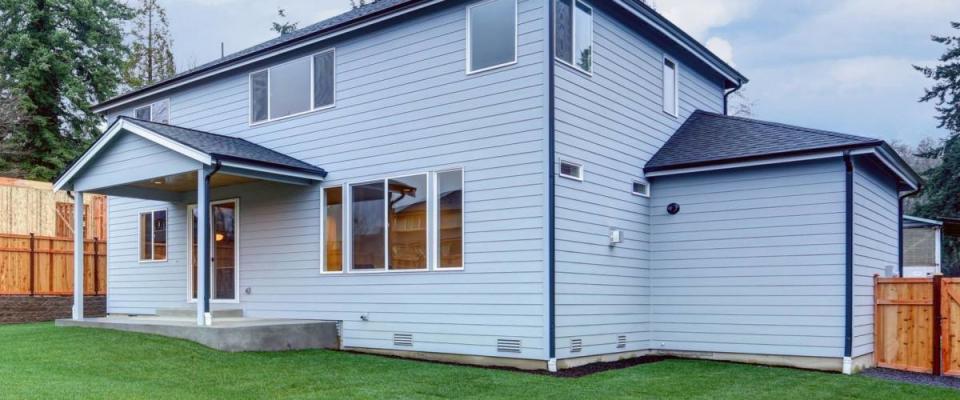 New luxury home with pale blue wood siding features covered back porch with wood plank ceiling over concrete floor. Fully fenced backyard boasts perfectly kept lawn. Northwest, USA