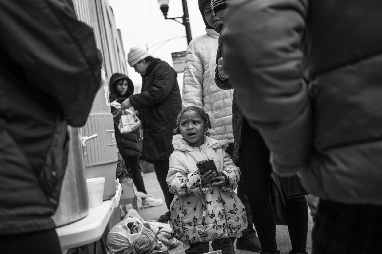 A little girl holds a cell phone as migrants wait in line for oatmeal. (Sebastian Hidalgo for NBC News)