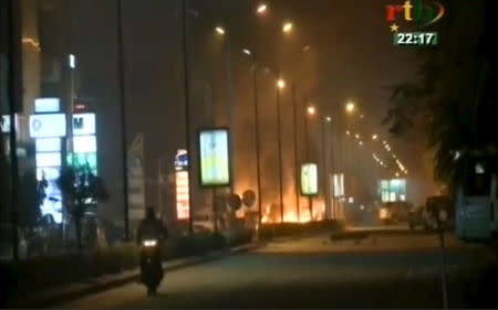 A motorcyclist rides along a road while fire and smoke rising from Splendid Hotel in Ouagadougou where suspected Islamist fighters are holding hostages in this still image from a video grab, January 15, 2016. REUTERS/RTB via REUTERS