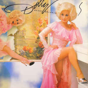 Dolly Parton propping up her leg dressed in a light pink ruffled, sheer dress with a high leg slit.