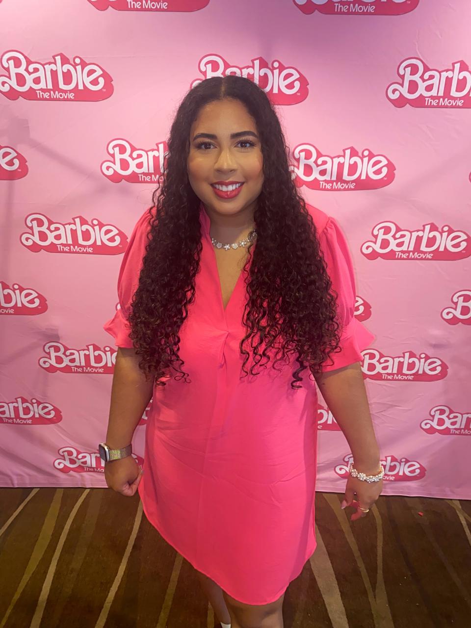 Melissa in hot pink dress in front of "Barbie" movie photo backdrop.