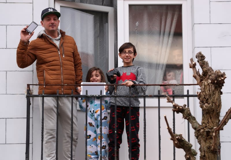 Resident Fernando and his children Enzo and Louna pose on the balcony of their home with objects significant to them during a coronavirus lockdown imposed by the Belgian government, in Brussels