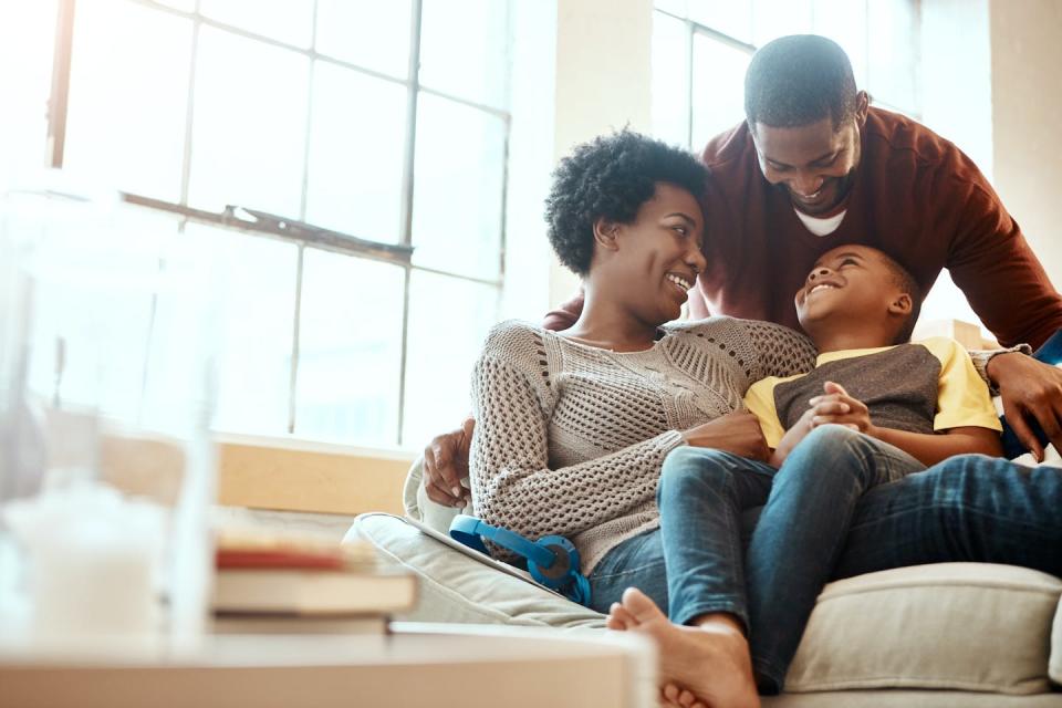 Parents seen cuddling and laughing with a child on a couch.