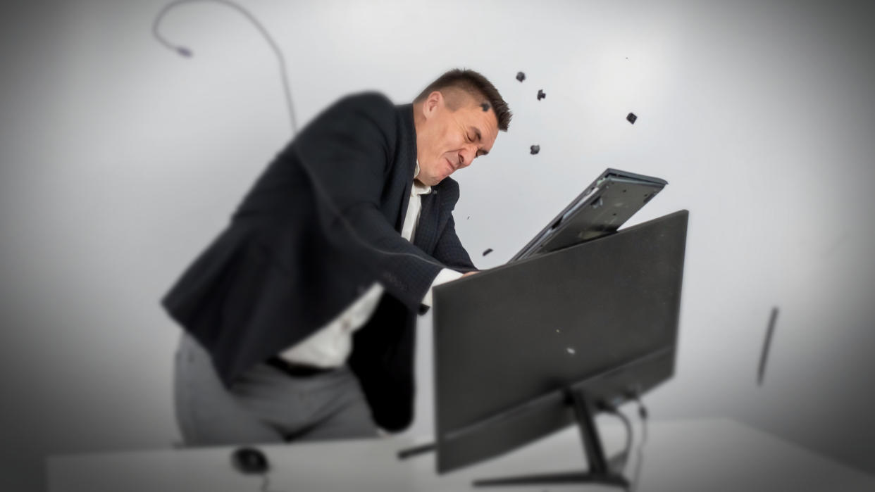   man in a suit gets angry and smashes the keyboard on the monitor 