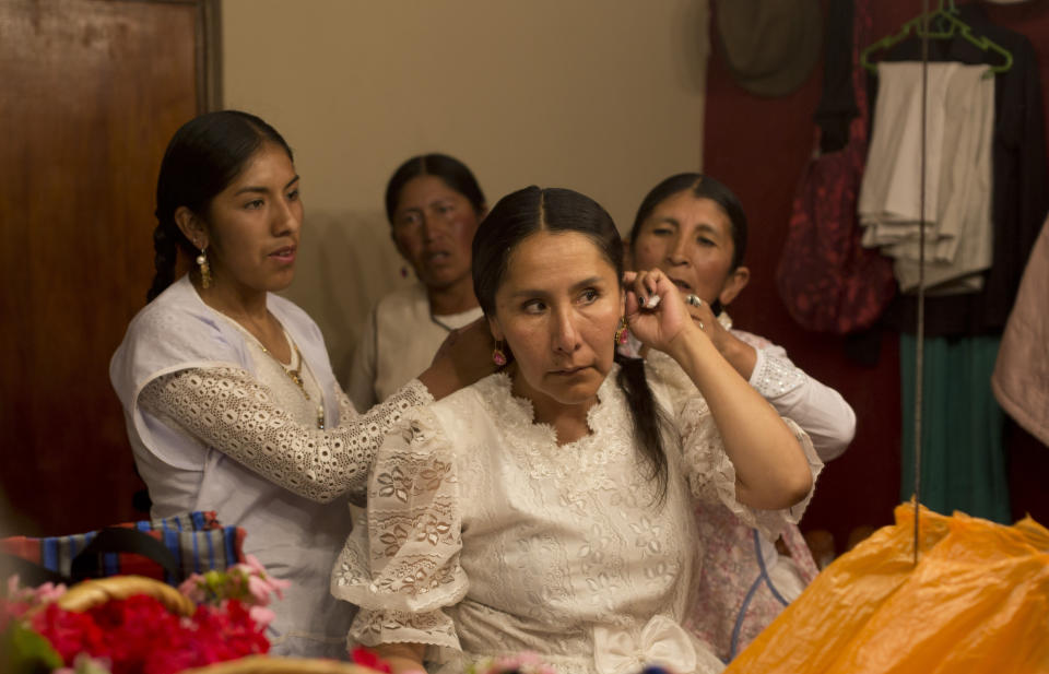 En esta imagen del 30 de abril de 2019, reflejada en un espejo, miembros de la compañía de teatro "Kory Warmis" o Mujeres de oro ayudan a su directora, Erika Andia, a prepararse para su actuación en el Teatro Municipal de La Paz, Bolivia. (AP Foto/Juan Karita)