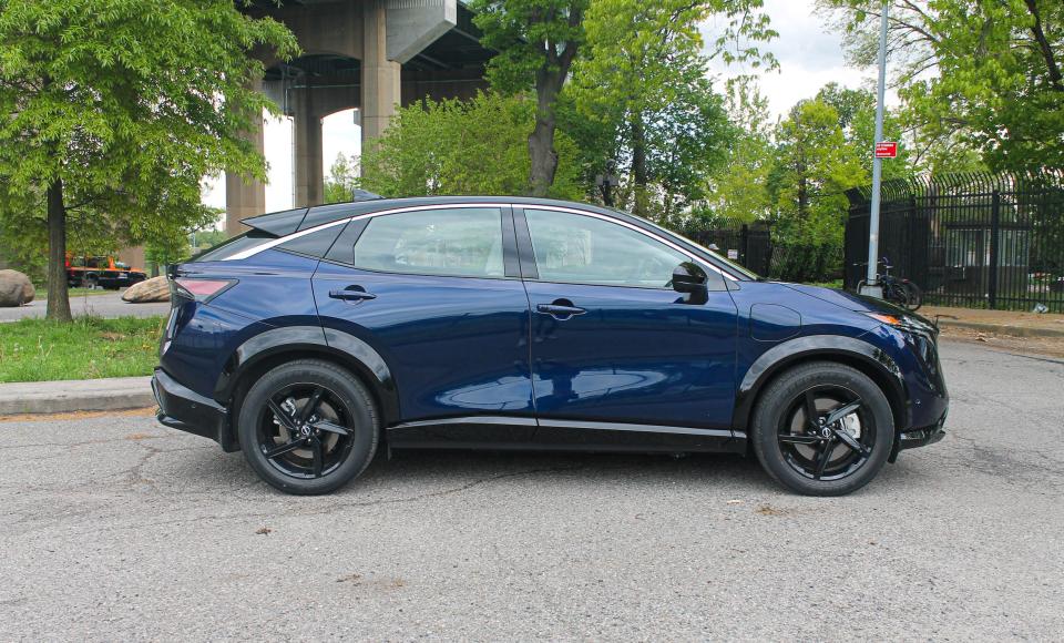 A blue Nissan Ariya electric SUV with trees in the background.