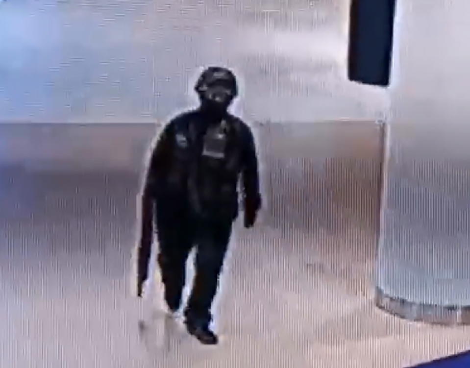 A CCTV still of the suspected gunman carrying a firearm with dark clothing and face coverings on.