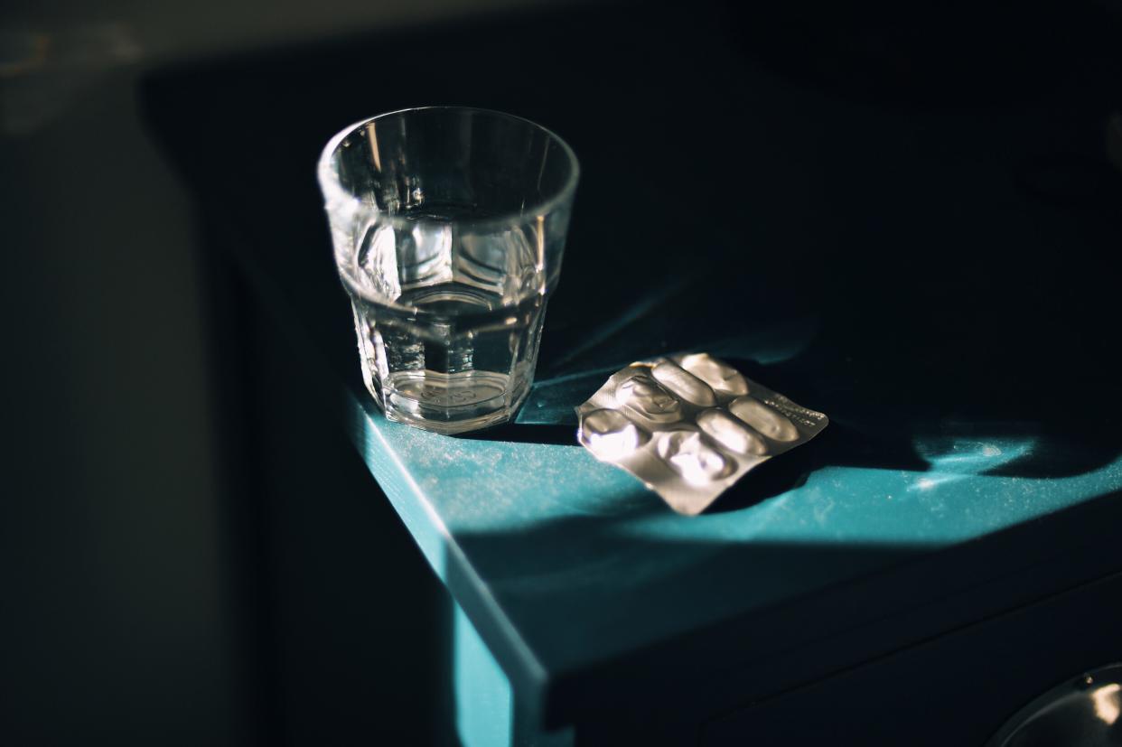 Glass of water and pills on bedside table. 