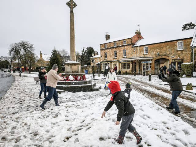 Families have a snowball fight on the High Street in Broadway (PA)