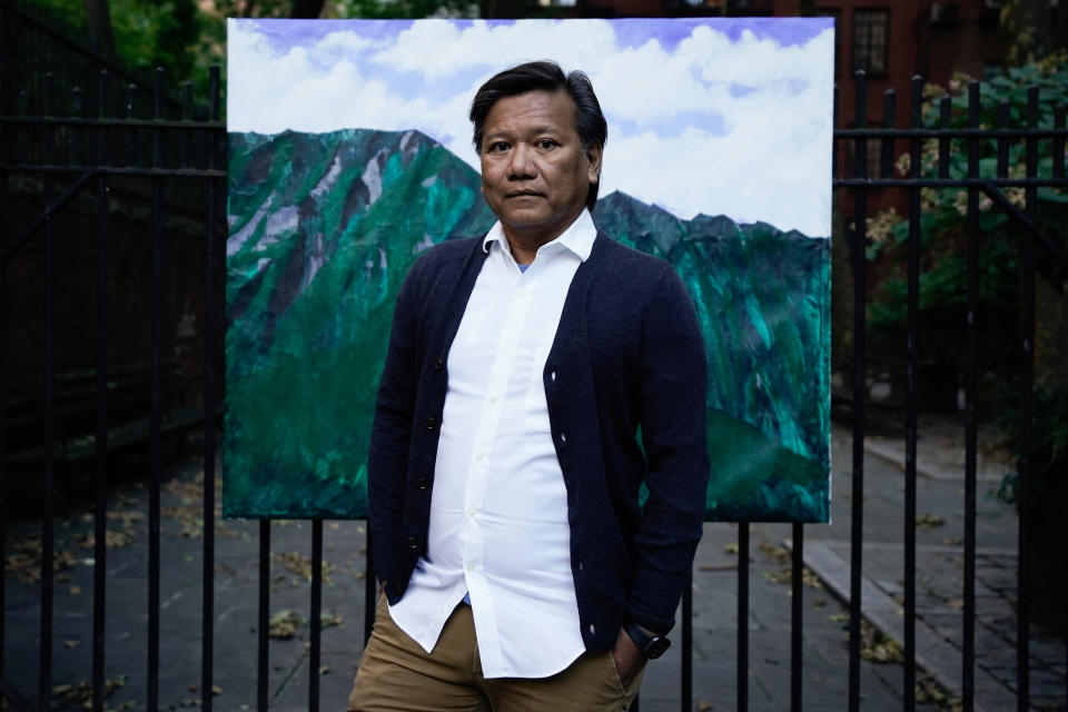 Bobby Calvan poses in front of a painting of the view from his childhood home in Waimanalo, Hawaii, Sunday, Oct. 9, 2022, in New York. His journey out of the closet has taken decades. Now 57, he is still sharing his truth about his sexuality. The journey hasn’t ended; indeed, it’s just beginning as he now lives his life as the man he believes he was meant to be. (AP Photo/Julia Nikhinson)