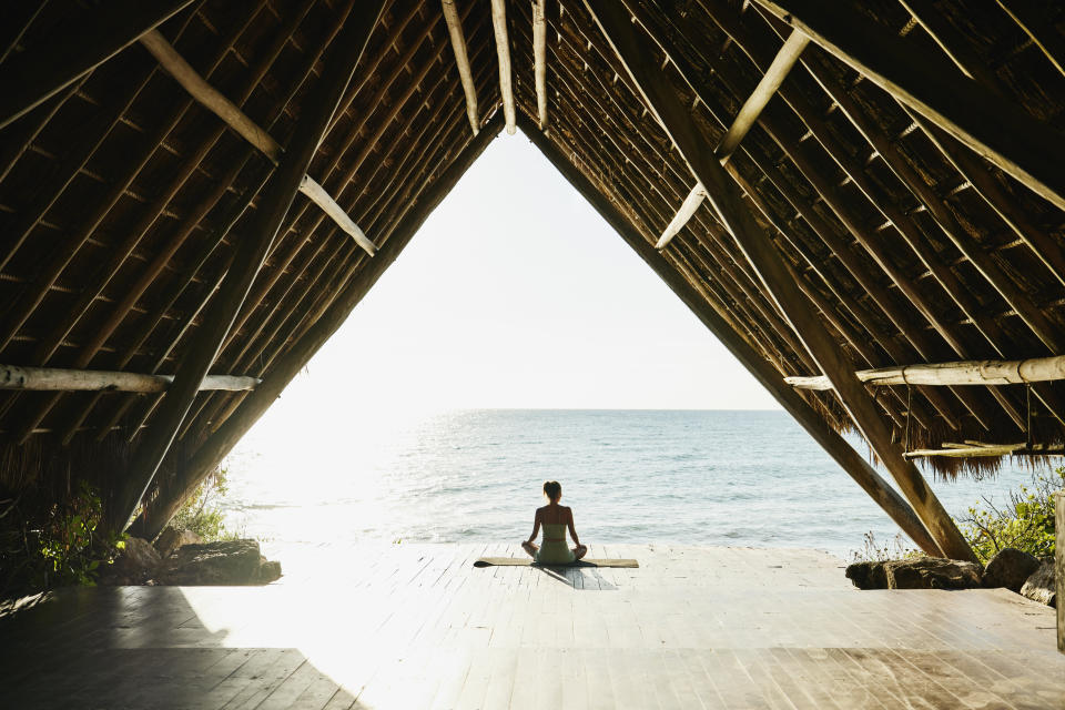 Mujer relaj&#xe1;ndose despu&#xe9;s de practicar yoga en el pabell&#xf3;n frente al mar en un resort tropical (Thomas Barwick via Getty Images)