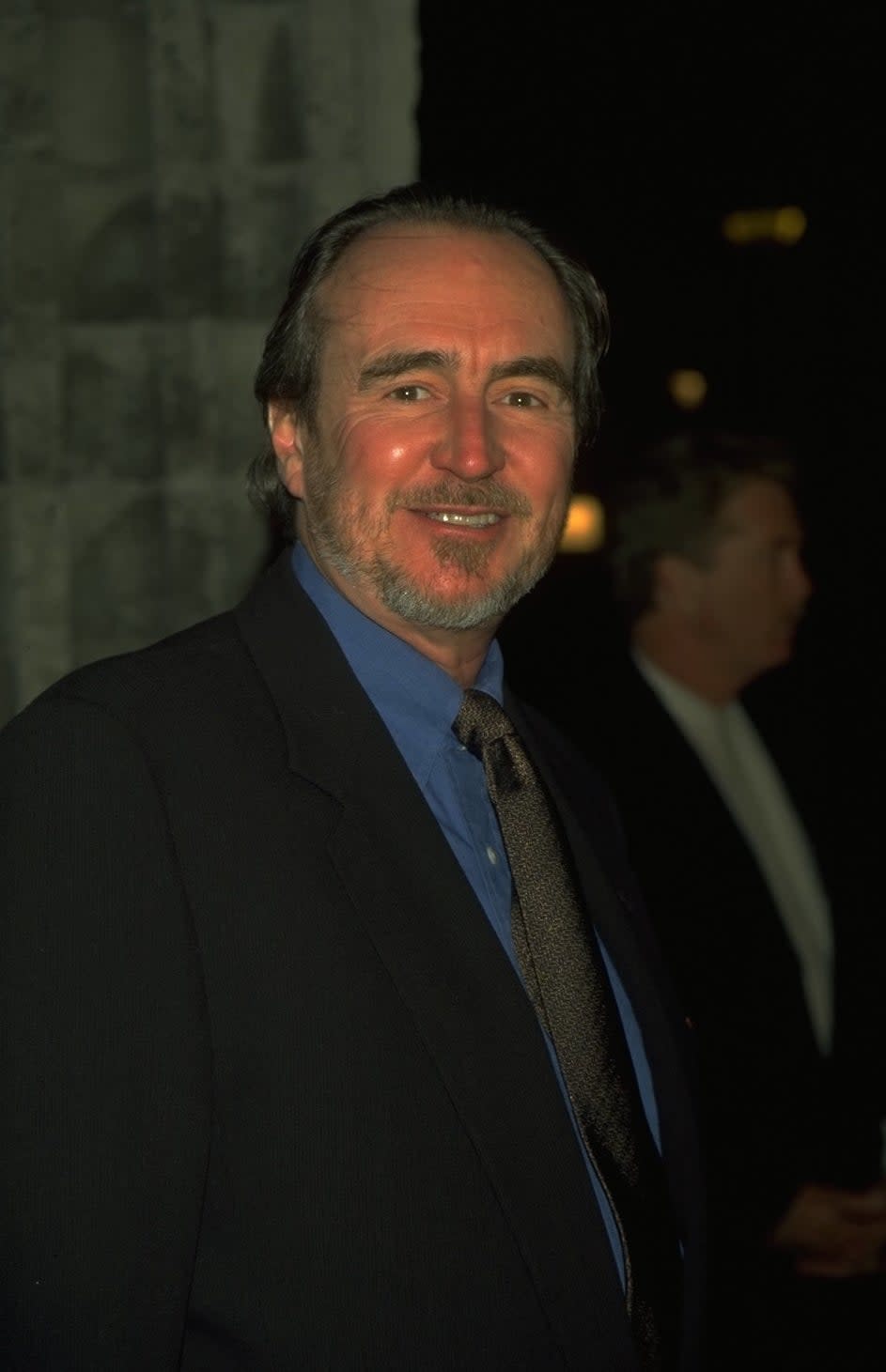 Wes Craven in a black suit with a blue shirt and black tie