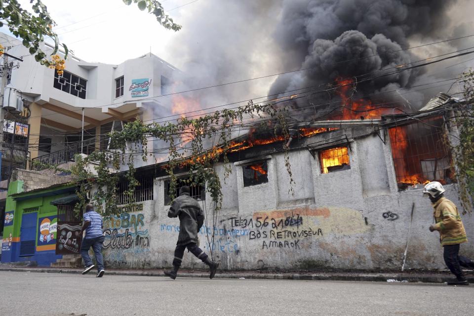 Bomberos corren a un restaurante que fue incendiado durante una protesta para exigir la renuncia del presidente Jovenel Moïse en Puerto Príncipe, el viernes 27 de septiembre de 2019. (AP Foto/Edris Fortune)