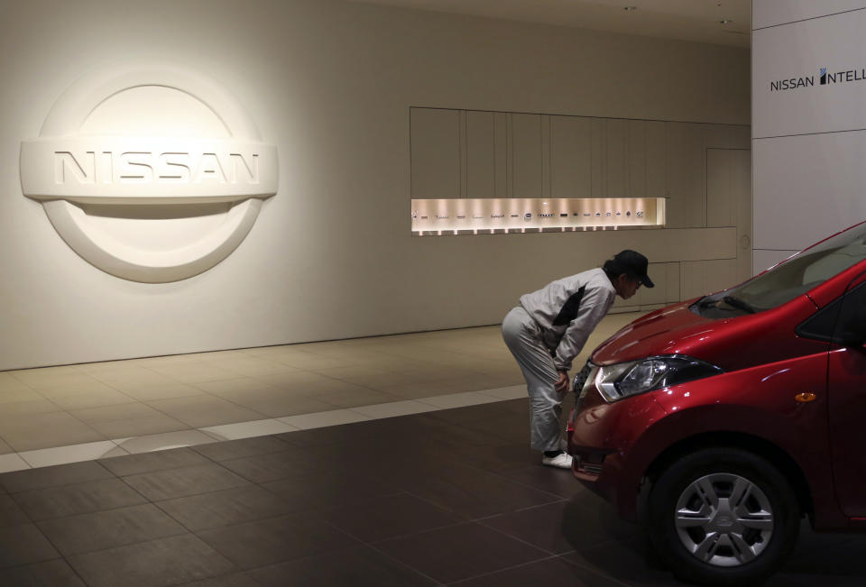 A man inspects car in front of the logo of the Nissan Motor Co. at its global headquarters in Yokohama, near Tokyo, Monday, Dec. 17, 2018. Nissan's board met Monday but failed to pick a new chairman to replace Carlos Ghosn, arrested last month on charges of violating financial regulations, saying more discussion was needed. (AP Photo/Koji Sasahara)