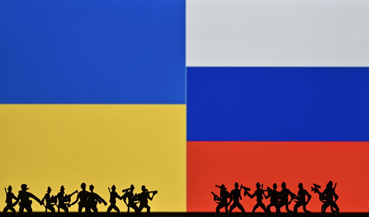 Illustrative photo of small figures of soldiers representing two armies in front of the flags of Ukraine and Russia