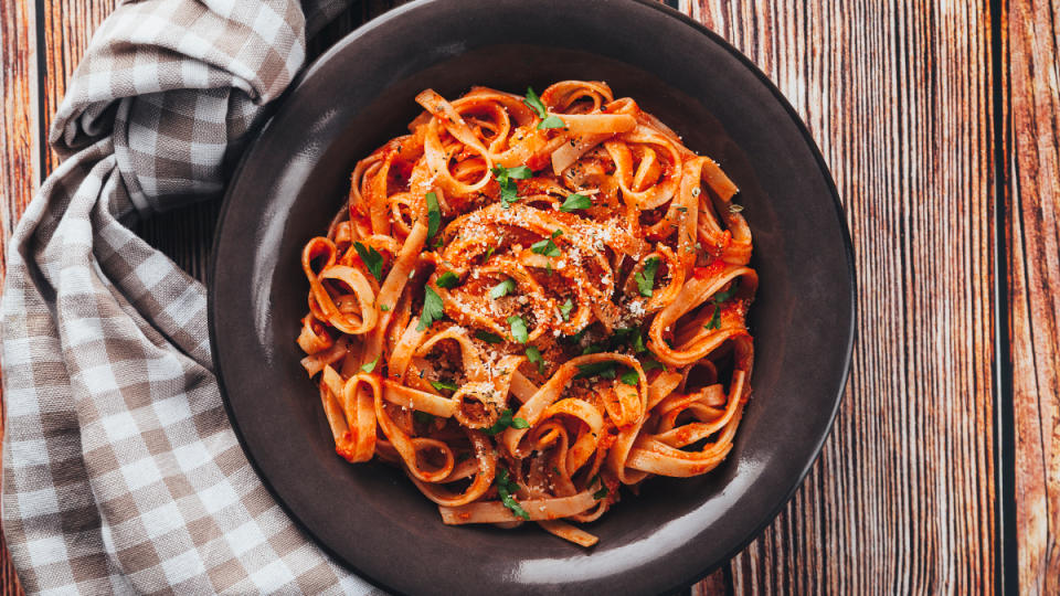 A bowl of pasta with tomato sauce on a wood table with a checkered kitchen towel