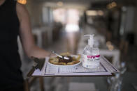 A waitress carries menus and hand sanitizer at a seafood restaurant in Marseille, southern France, Tuesday, June 2, 2020. The French way of life resumes Tuesday with most virus-related restrictions easing as the country prepares for the summer holiday season amid the pandemic. (AP Photo/Daniel Cole)