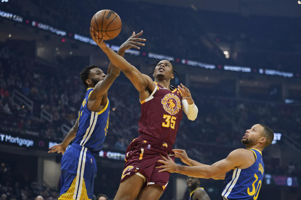 Cleveland Cavaliers' Isaac Okoro (35) drives to the basket against Golden State Warriors' Andrew Wiggins (22) and Stephen Curry (30) in the first half of an NBA basketball game, Thursday, Nov. 18, 2021, in Cleveland. (AP Photo/Tony Dejak)