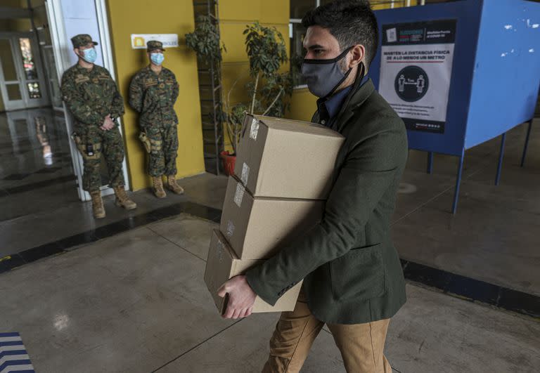 Un trabajador carga una caja con alcohol en gel adentro de uno de los centros de votación en Santiago de Chile