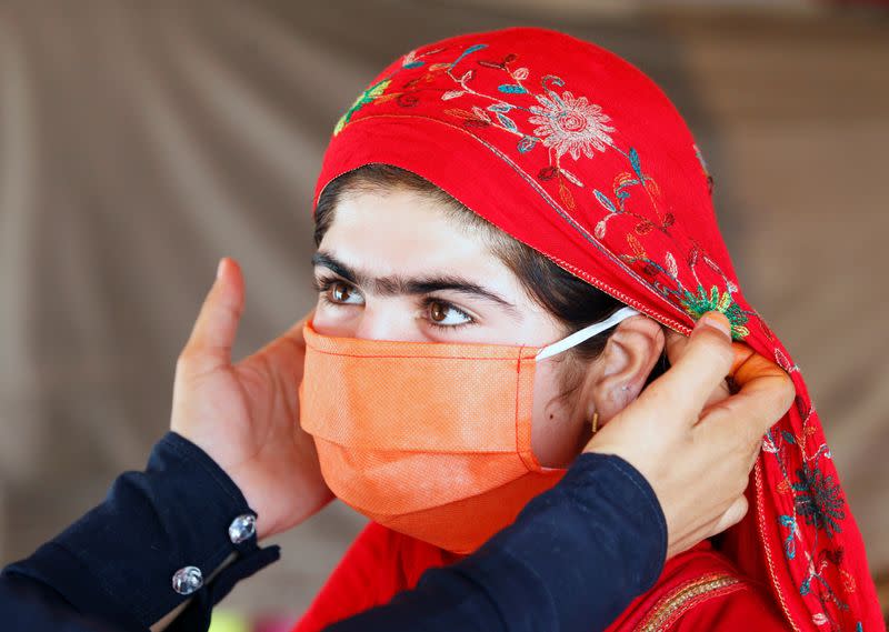 FILE PHOTO: A UNICEF worker helps an internally displaced girl put on a face mask at a makeshift camp, amid the coronavirus disease (COVID-19) outbreak, in Jalalabad