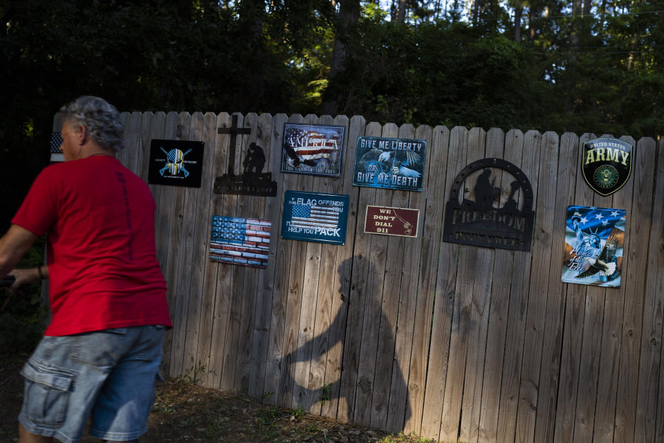 Robert Rohde mows the lawn past a fence adorned with pro-America signs at his home in Flint, Texas, Friday, June 9, 2023. This is a place where people believe deeply in the Second Amendment, that guns are fundamental to the identity of the nation, that guns protect their families. (AP Photo/David Goldman)