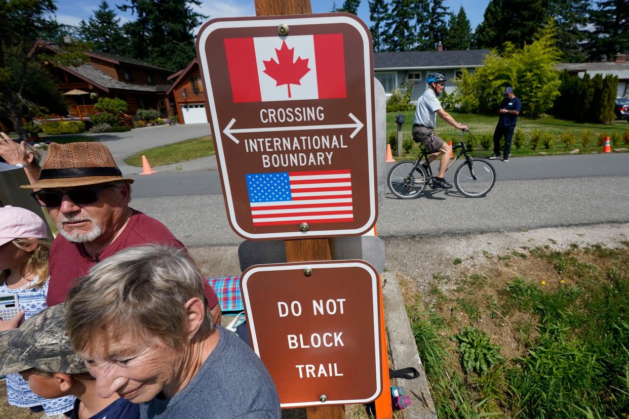 A family visits across the U.S.-Canada border at the Peace Arch Historical State Park as a cyclist rides past on the Canadian side, Monday, Aug. 9, 2021, in Blaine, Wash. 