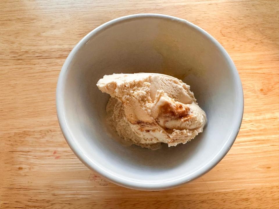A white bowl of a light-brown ice cream with a darker brown caramel swirled into the scoop